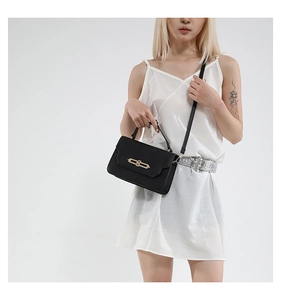 Detail of elegant black matte crossbody bag with golden clasp worn with white dress