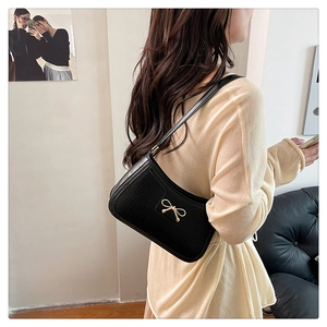 Detail of black faux crocodile skin shoulder bag with golden bow metallic buckle hardware