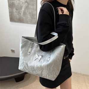 Metallic silver tote bag with butterfly buckle shown on model in a minimalist setting