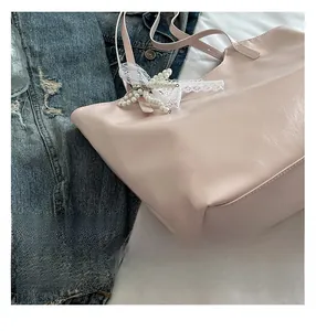 Detail of light pink tote bag with white lace bow and pearl charm on a soft background