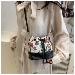 Detail of floral tapestry bucket bag featuring black leather trim and drawstring closure