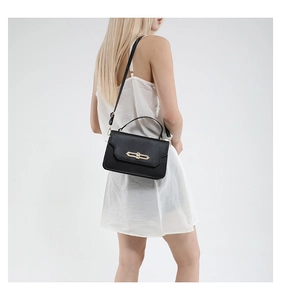 Detail of a black matte leather handbag with gold rectangular clasp and crossbody strap