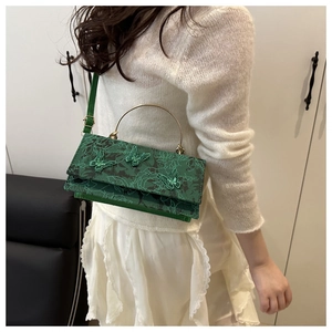 Detail of green butterfly embroidery on lace textured crossbody bag with gold metal handle