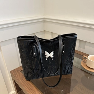 Elegant black tote bag with silver butterfly accent and pleated texture on a table