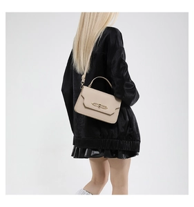 Model wearing a beige leather handbag with a golden lock and geometric flap design