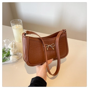 Détail du nœud argenté sur un sac porté épaule marron à motif crocodile sur table