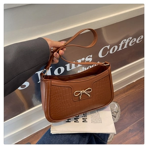 Détail d'un sac baguette marron aspect croco avec un nœud en métal doré