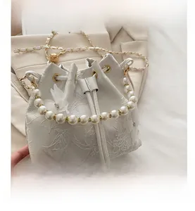 Detail of white lace bucket bag featuring floral texture and large pearl handle