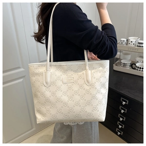 Detailed view of a white floral embossed tote bag carried by a model over shoulder
