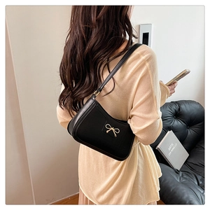 Detail of black glossy leather underarm bag with gold bow clasp on a model shoulder