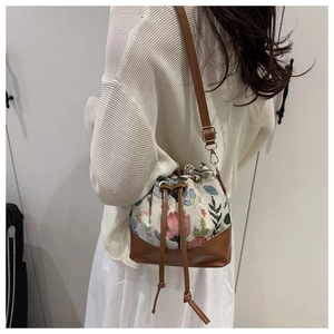 Detail of floral embroidery and brown leather trim on a vintage drawstring bucket bag