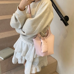 Minimalist light pink leather bucket bag with croissant charm on a modern grey staircase