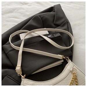 Detail shot of white croc-embossed underarm bag with gold chain on dark blazer
