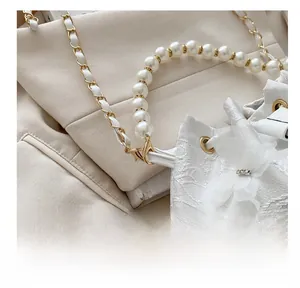 Detailed view of pearl handle and gold metal hooks on white textured fabric bag