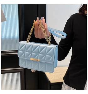 Detail of light blue quilted crossbody bag with gold chain and metal buckle closure