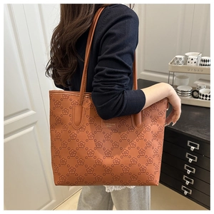 Large capacity brown tote bag with embossed floral pattern on model's shoulder.