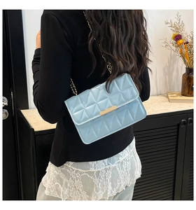Detail of light blue quilted leather bag with gold chain strap worn by a model