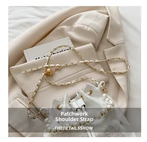 Detail of white lace bucket bag with pearl handle and golden butterfly ornament