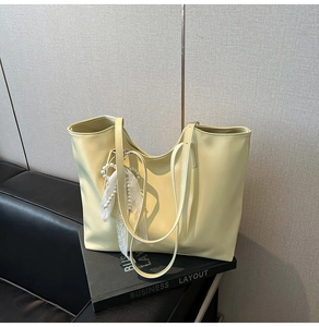Close-up of cream yellow tote bag with pearl and lace bow charm on black leather couch