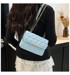 Detail of light blue quilted crossbody bag with gold chain strap shown on model's shoulder