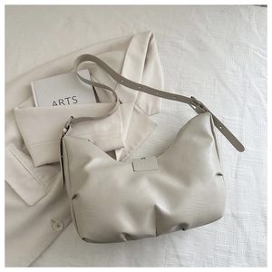 Detail of cream pleated crescent bag with adjustable strap on a minimalist background