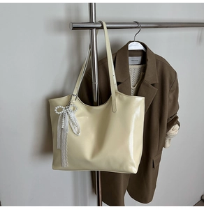 Detail of cream tote bag with pearl bow and lace charm on a clothing rack