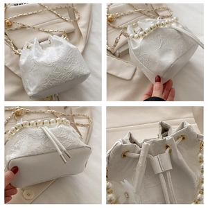 Detail view of white jacquard bucket bag with pearl handle and golden chain strap
