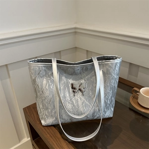 Borsa tote argento con trama stropicciata e logo a farfalla su tavolo in legno
