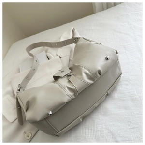 Detail of creamy white crossbody bag showing pleated leather texture and metal rivets