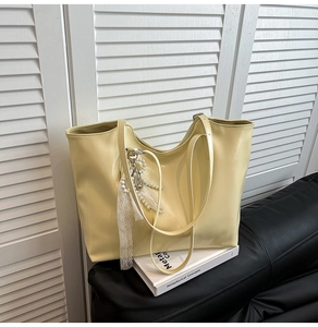 Dettaglio di una borsa tote beige con ciondolo decorativo in perle e pizzo su pelle