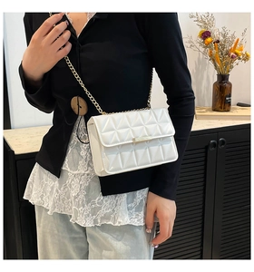 Close-up of white quilted crossbody bag with gold metal chain strap and twist lock detail