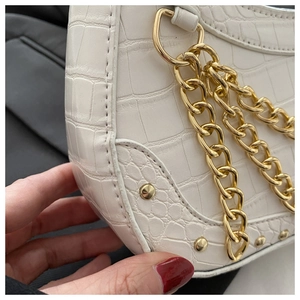 Close-up of white crocodile pattern shoulder bag with chunky gold chain and metal rivets