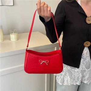 Sac sous le bras rouge à motif crocodile avec nœud doré présenté dans un cadre d'intérieur