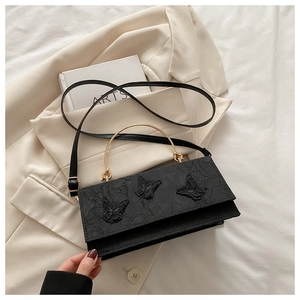 Detail of black crossbody bag featuring 3D butterfly appliques and gold metal handle