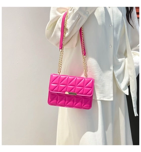 Detail of rose pink quilted crossbody bag with gold chain strap on white outfit