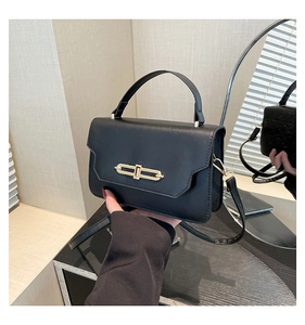 Close-up of black matte leather handbag featuring a sleek gold bar lock and top handle
