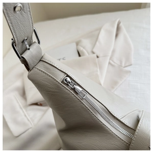 Close-up of beige leather bag showing silver metal zipper and adjustable strap details