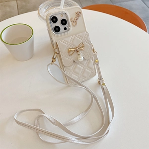 Dettaglio della custodia iPhone bianco crema con fiocco, ciondolo di perla e tracolla regolabile