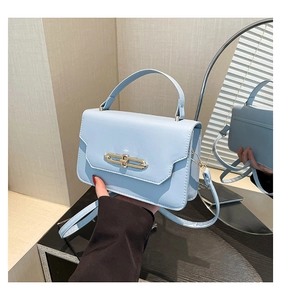 Detail of light blue PU leather bag with gold geometric buckle and handle reflecting in a mirror