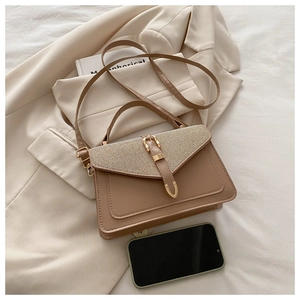 Detail view of khaki crossbody bag on a beige blazer with golden metal buckle and strap