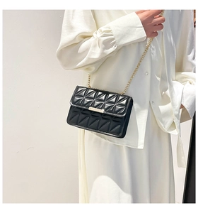 Detail of black quilted crossbody bag with gold chain and metal buckle on white shirt