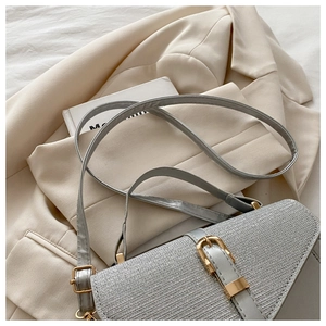 Detail of silver-grey crossbody bag with gold metal buckle on a white blazer