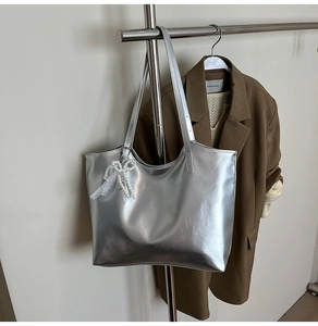 Detailed view of silver metallic tote bag with pearl lace bow charm on thin shoulder strap