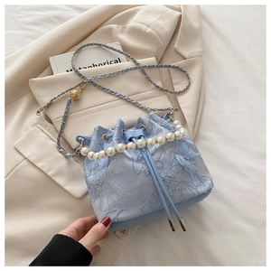 Detail of light blue lace embroidery bucket bag with pearl handle on beige blazer