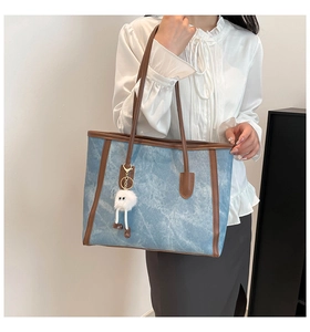 Nahaufnahme einer blauen Tragetasche in Denim-Optik mit braunem Rand und Anhänger.