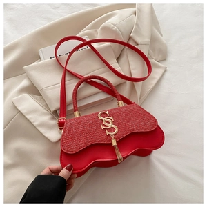 Détail macro du sac rouge avec logo doré, pompon métallique et base ondulée