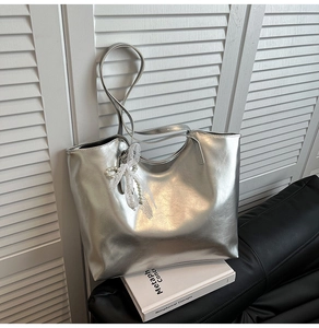 Dettaglio borsa tote argento a specchio con fiocco in pizzo bianco e ciondolo di perle