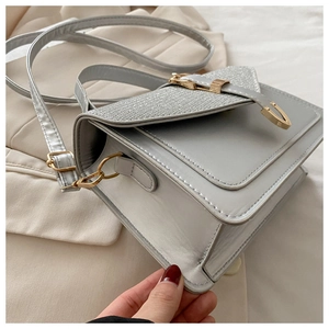 Detail of grey crossbody bag with silver glitter flap and gold metallic lock closure