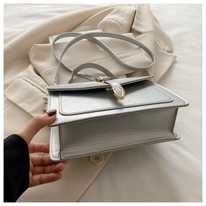 Detail of silver faux leather crossbody bag with gold metal buckle on white blazer