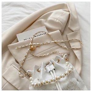 Detail of white bucket bag featuring 3D floral accents and elegant pearl handle